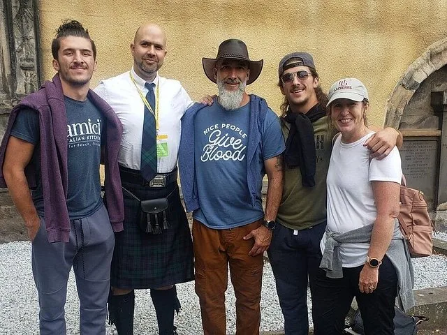 Un groupe de cinq personnes pose pour une photo près d'un mur en pierre.