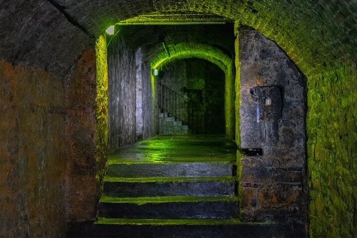 Ein dunkler, grün beleuchteter Steintunnel mit Treppen im Inneren.